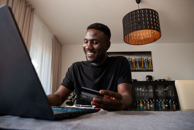 Smiling man holding credit card using laptop at home