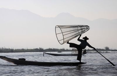 Silhouette man on boat in lake against sky