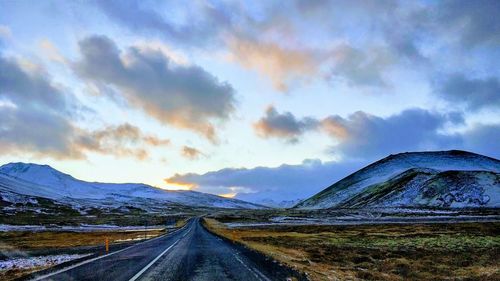 Empty road leading towards mountains against sky