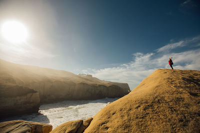 Side view of woman standing on cliff by sea against sky