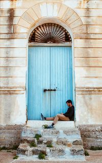 Man sitting in front of a closed door of an abandoned building at the beach