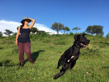 Young woman with dog standing on field against clear sky