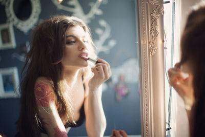 Young woman applying lipstick reflecting in mirror