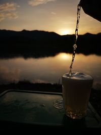 Close-up of drink pouring water in glass during sunset