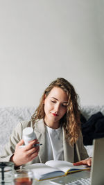 Young woman using mobile phone while sitting on table against white background