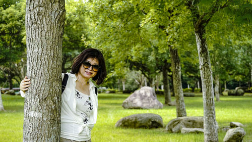 Portrait of smiling woman standing by tree trunk