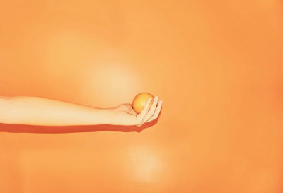 Cropped image of woman holding fruit against orange background