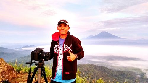 Young man photographing on mountain against sky