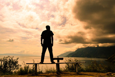 Rear view of silhouette man standing by lake against sky
