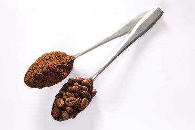 High angle view of ground coffee and beans in spoons over white background