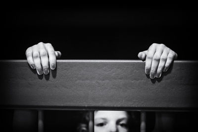 Close-up of hands on railing with girl against black background