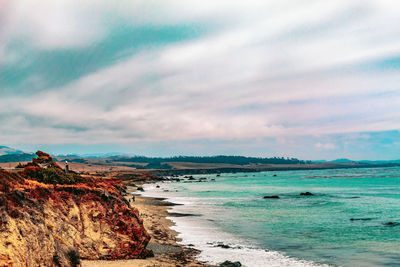 View of calm beach against cloudy sky