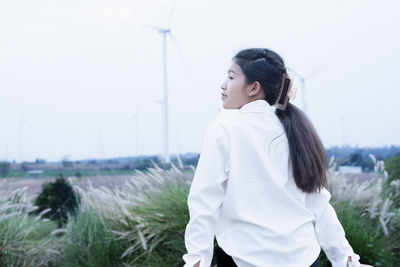 Side view of young woman standing against sky