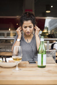 Woman wearing headphones while listening music from mobile phone at sidewalk cafe table