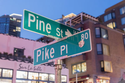 Low angle view of road signs by buildings in city at dusk