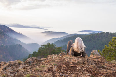 Woman hiker on a mountain top looking to low clouds and hills breaking through