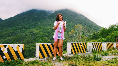 Portrait of smiling woman gesturing while standing against green mountain during foggy weather