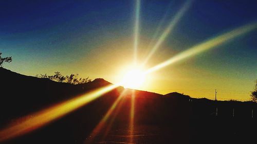 Sun shining over silhouette landscape against sky during sunset