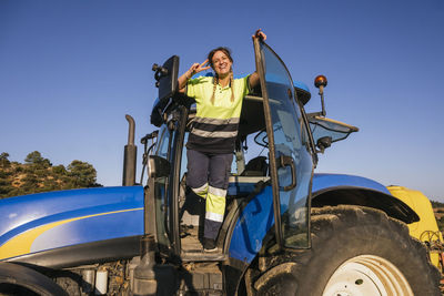 Happy female farmer gesturing peace sign standing in tractor