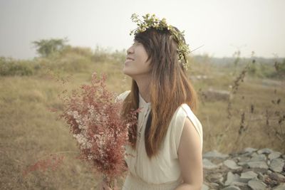 Smiling young woman wearing flower wreath while standing on field