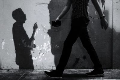 Low section of man walking on footpath by wall