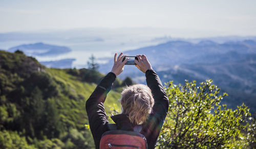 Woman photographing with smart phone against sky