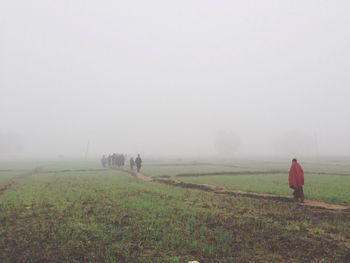 Rear view of people walking on field against sky during foggy weather