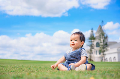 Cute boy sitting on field against sky