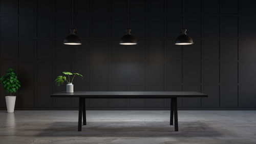 Illuminated pendant lights hanging over table against wall