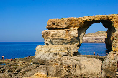 Rock formation by sea against clear blue sky