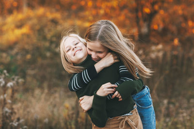 Two happy little girls sisters laughing, having fun and playing in the fall in nature outdoors 