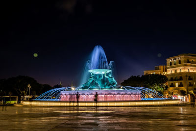 Illuminated fountain in city against sky at night
