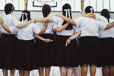 Female friends crossing fingers with arm around standing in school