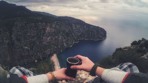 Midsection of man holding drink on mountain by sea