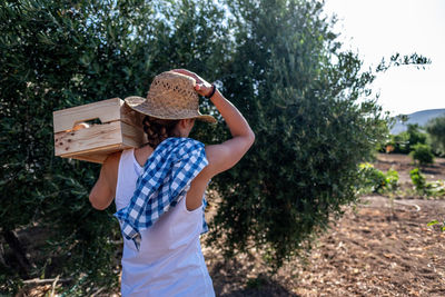Full length of woman holding hat standing against plants