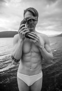 Midsection of shirtless man standing at beach against sky