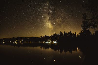 Silhouette trees by lake against sky at night