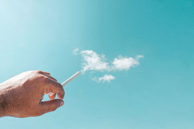 Man holding cigarette against blue sky