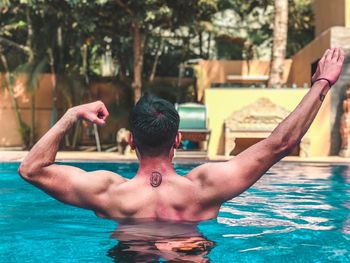 Rear view of shirtless man flexing muscles in swimming pool