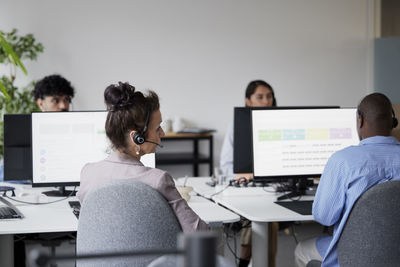 Rear view of businesswoman using headset in office in front of computer screen