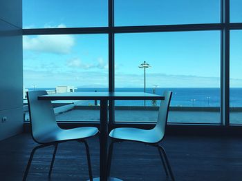 Chairs by sea against sky seen through window