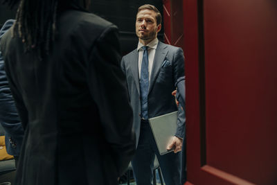 Young businessman holding laptop while discussing with male and female colleagues in hotel lounge