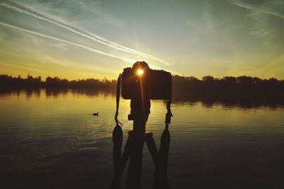 Camera at lakeshore against sky during sunset