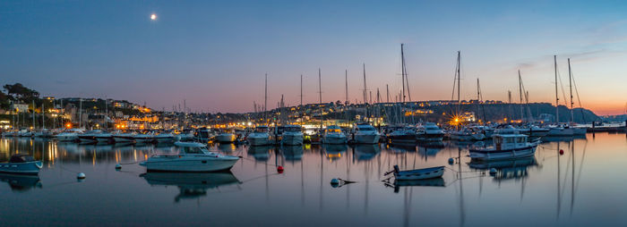 Sailboats moored in harbor at sunset