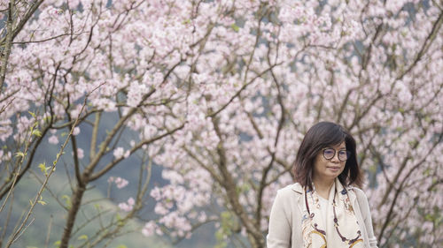 Portrait of young woman standing by cherry blossom tree