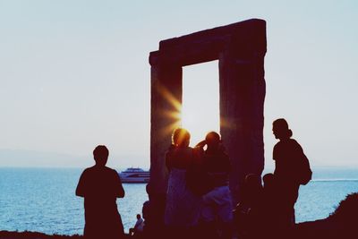 Silhouette people standing by sea against clear sky during sunset