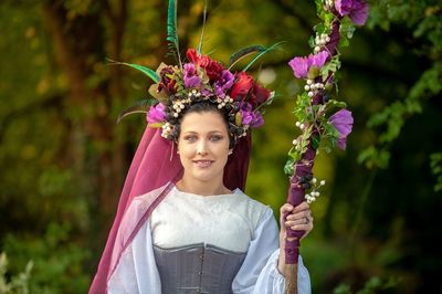 Portrait of smiling young woman standing by flowering plants