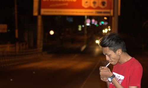 Man smoking cigarette while standing on road at night