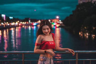 Young woman standing against railing at night
