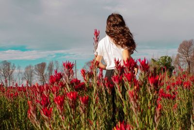 Woman standing by flowers on field against sky